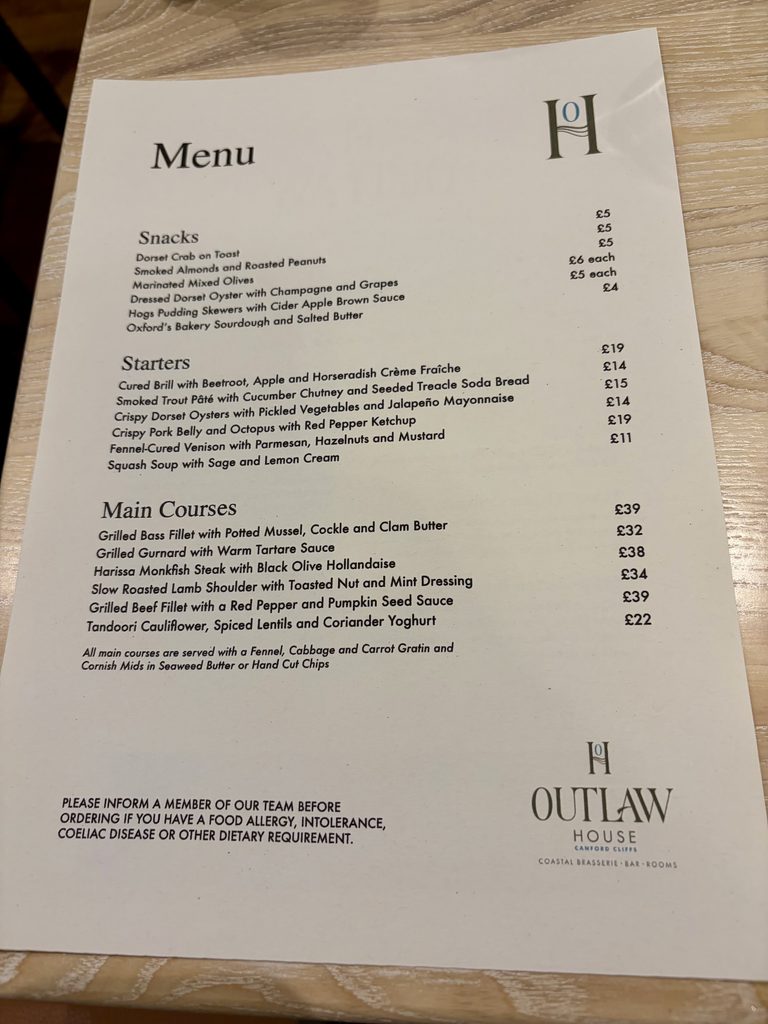 Food menu listing snacks, six starters and six main courses, on a pale wooden table