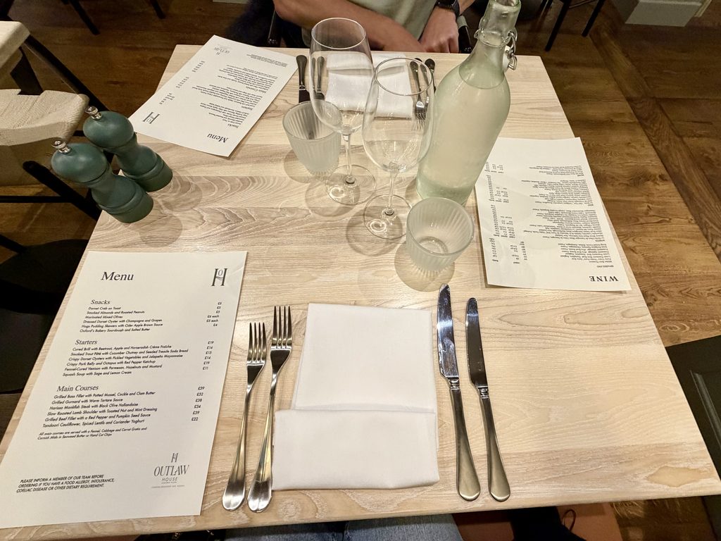 Table for two laid with menus, cutlery, napkins, wine glasses, a water bottle and green pepper mills