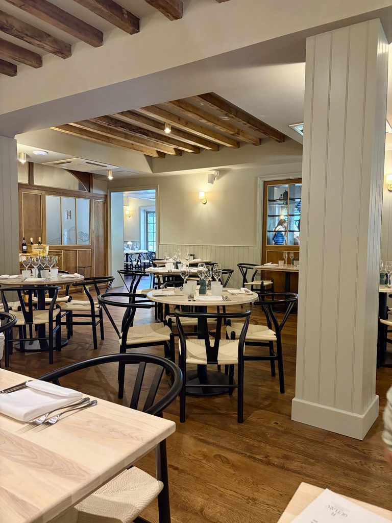 Dining room at Outlaw House with pale wood tables, black wishbone chairs and exposed ceiling beams