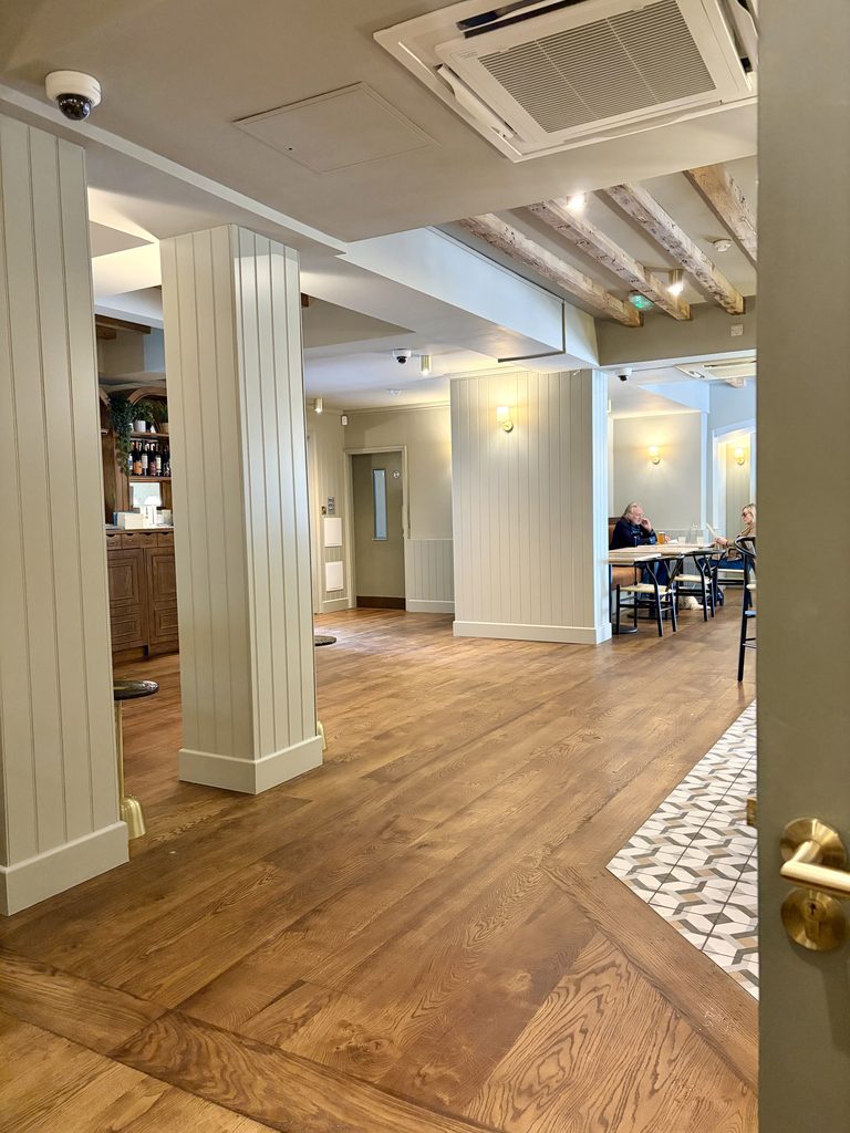Bar area with panelled pillars, an oak floor, a patterned tiled entrance and diners at the back