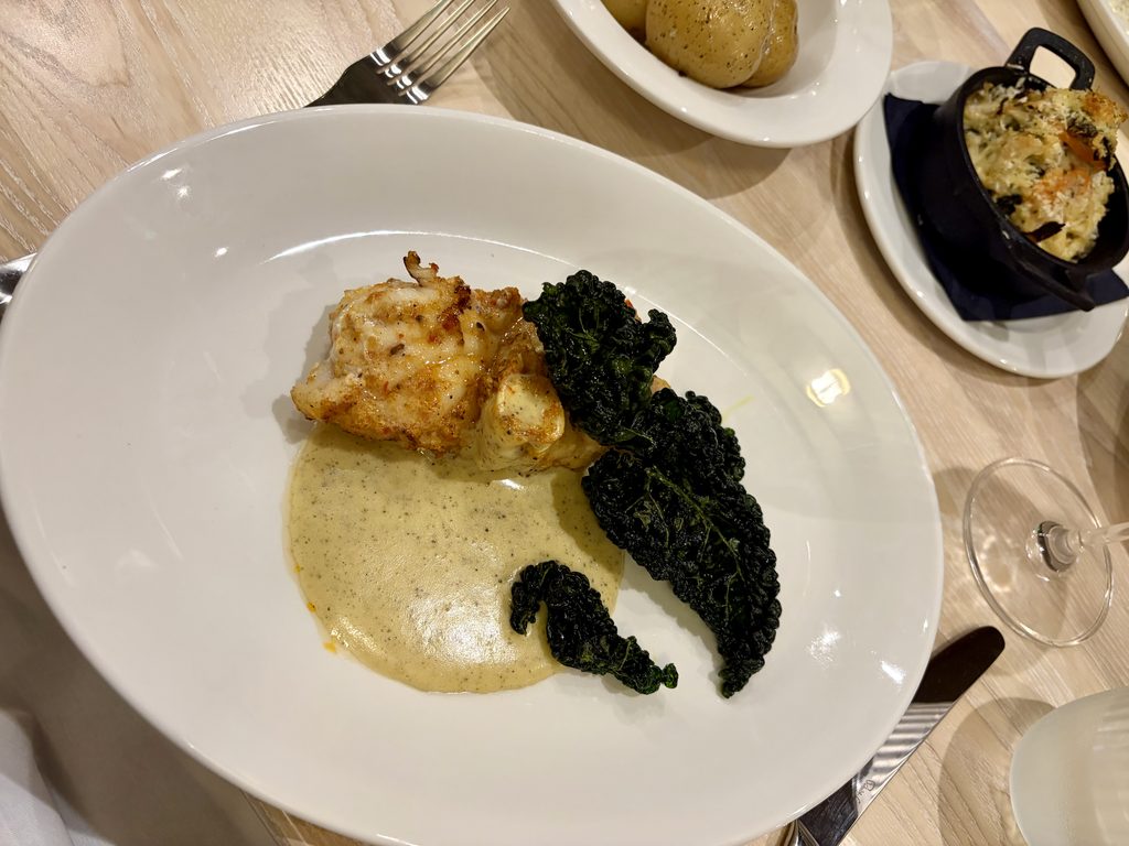 Harissa monkfish steak with black olive hollandaise and dark leafy greens, with side dishes behind
