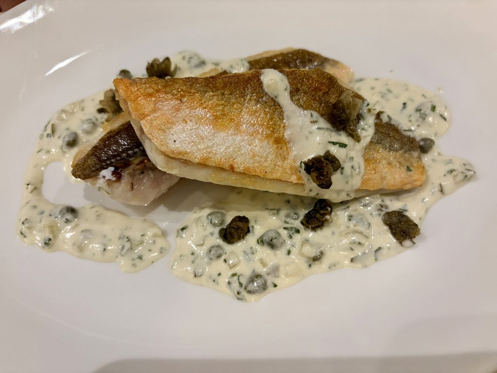 Grilled gurnard fillets with warm tartare sauce and crispy capers on a white plate