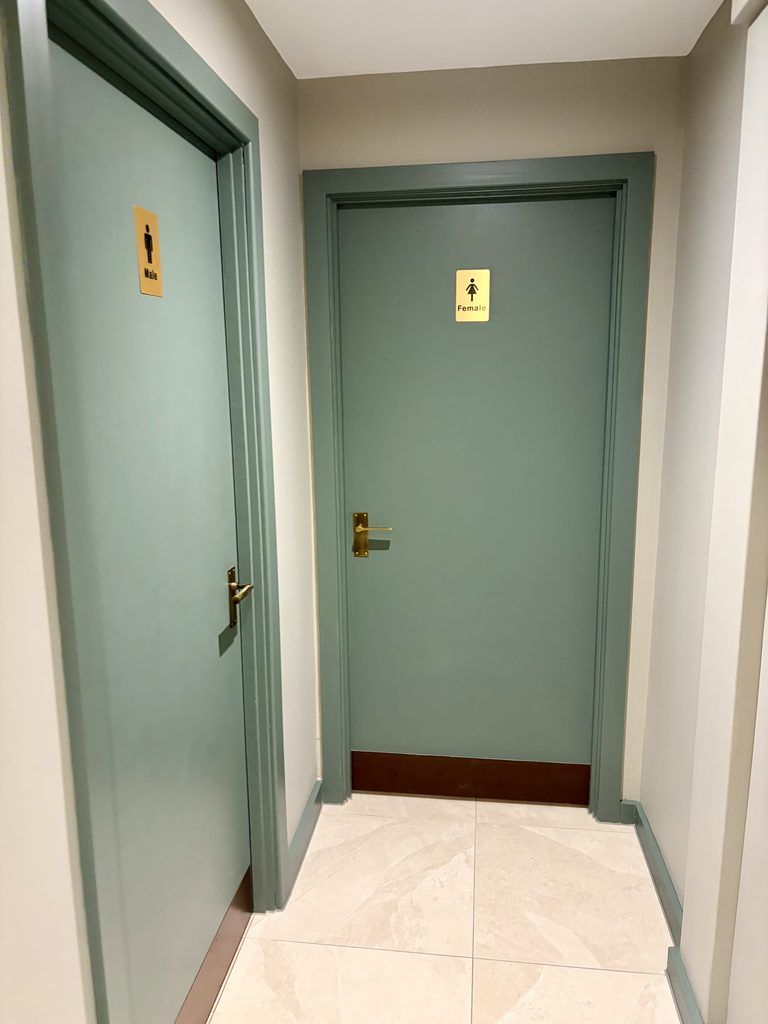 Corridor with two sage green toilet doors marked Male and Female, with brass signs and handles