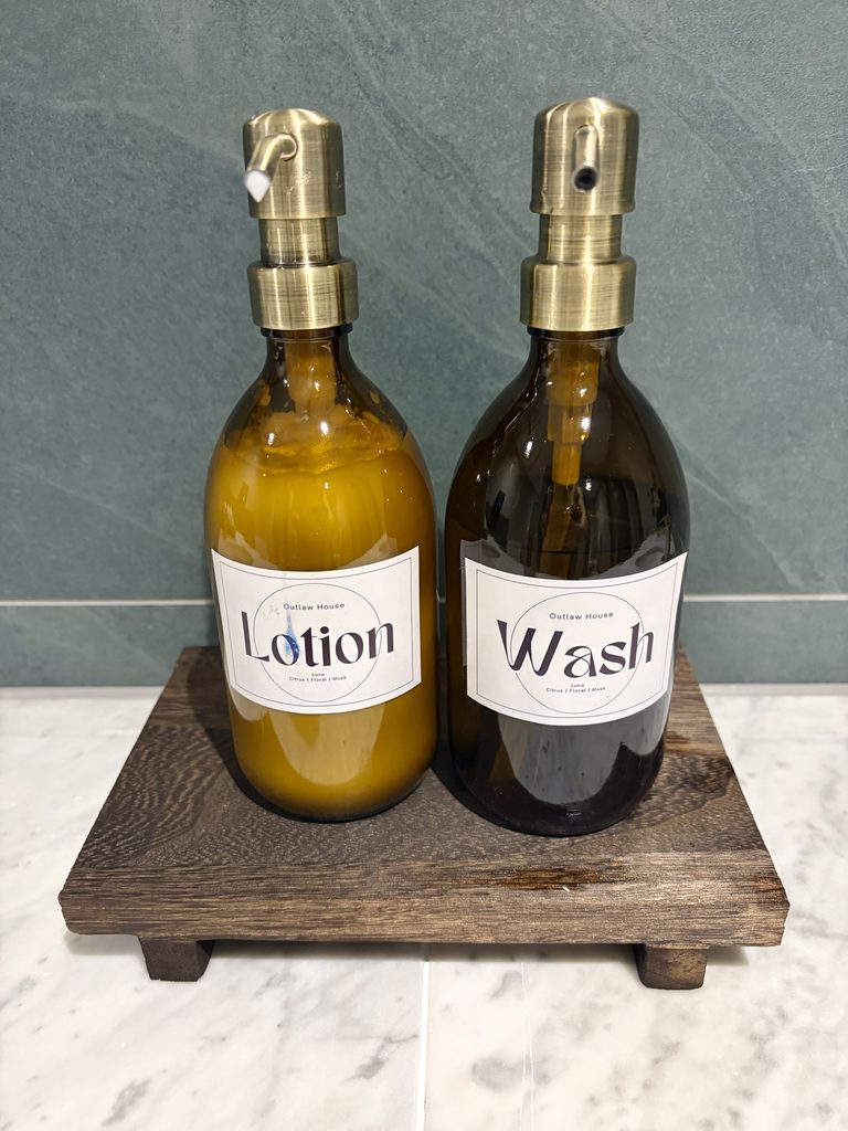 Lotion and hand wash in amber pump bottles with brass tops on a dark wooden stand