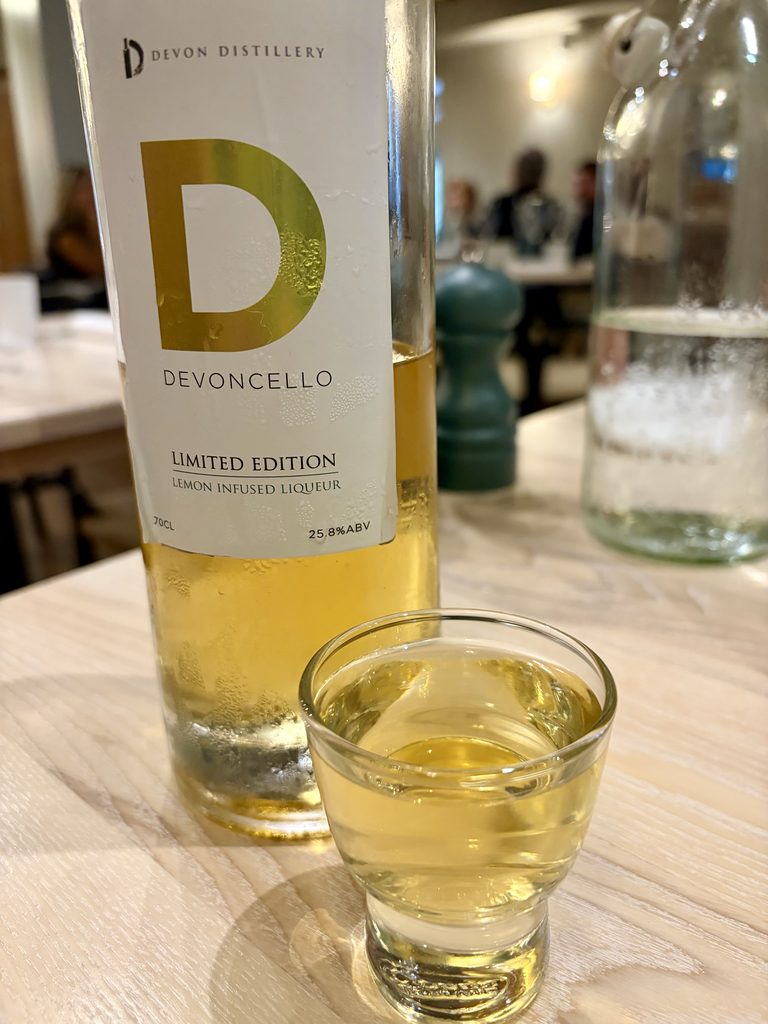 Bottle of Devoncello lemon liqueur with a small glass poured, on the table after the meal