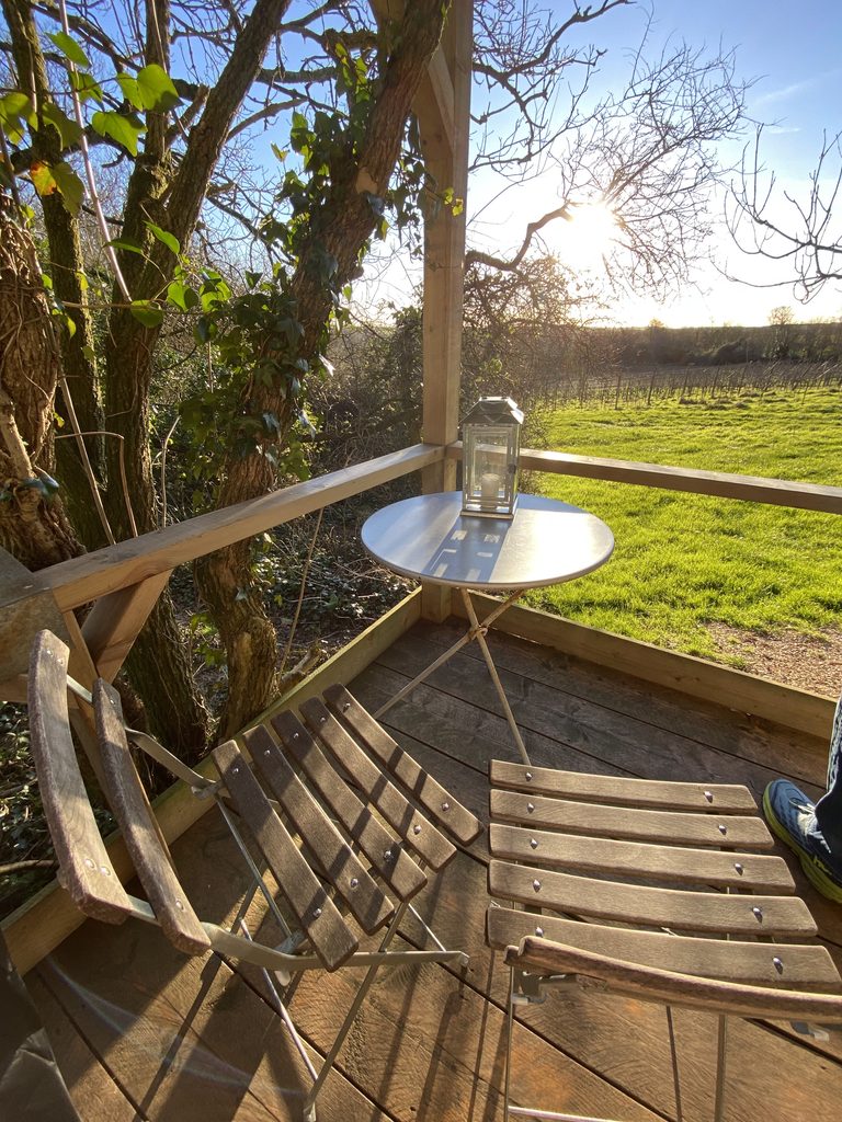Folding chairs and a bistro table with a lantern on the deck, looking over the vineyard in winter sun