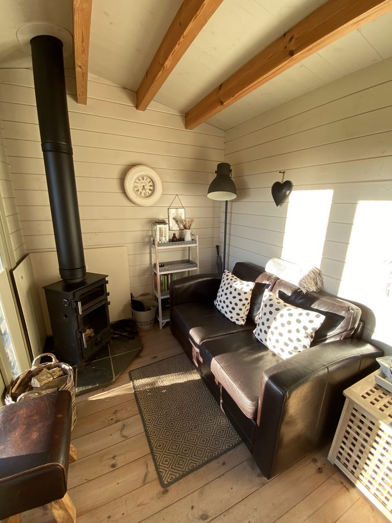 Cosy cabin living space with a wood burner, a leather sofa with spotted cushions and a wall clock