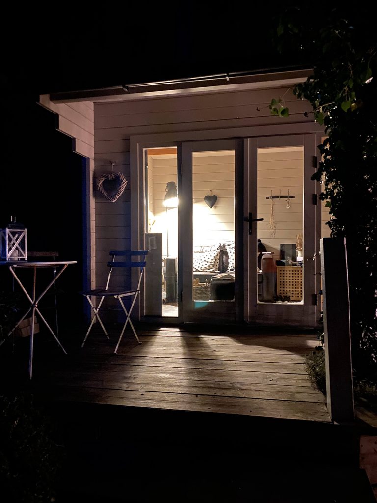 The cabin lit up at night, its sofa seen through the glass doors, with a bistro table on the deck